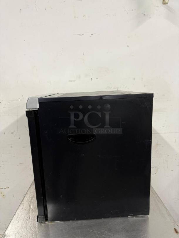 Black mini fridge with a simple handle, showing minimal wear. No visible branding or labels. Ideal for compact spaces.