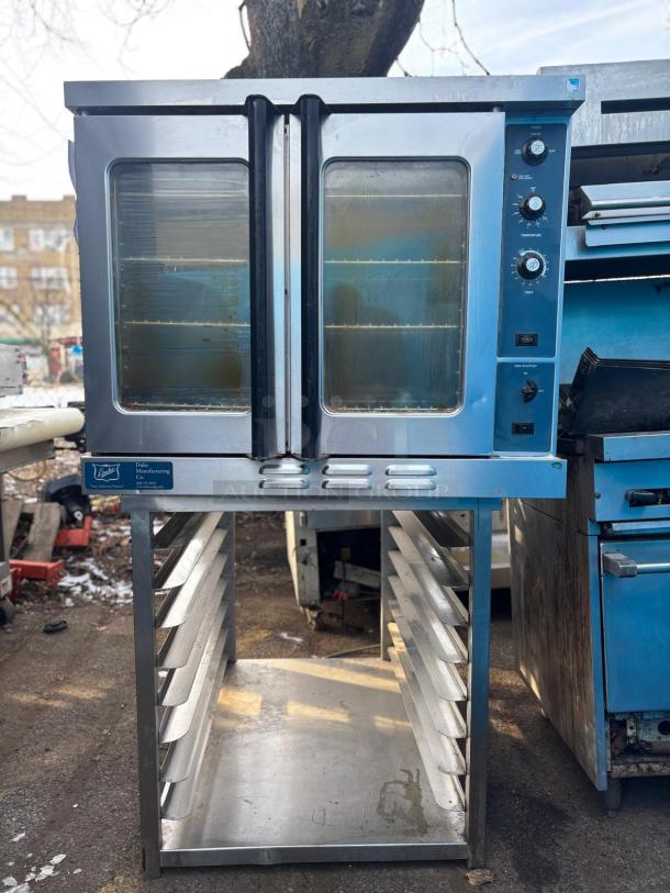 Commercial double-door convection oven by Duke Manufacturing, stainless steel, visible knobs and control panel, shelving unit below.