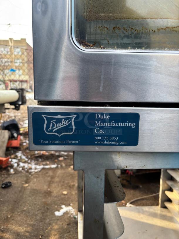 Duke Manufacturing stainless steel equipment with visible logo and contact details, showing some wear and rust on glass.
