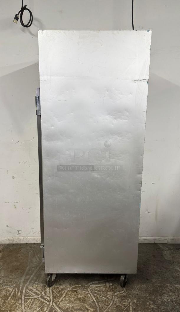 Commercial stainless steel refrigerator on wheels, showing side view; visible wear and scratches, power cord attached.
