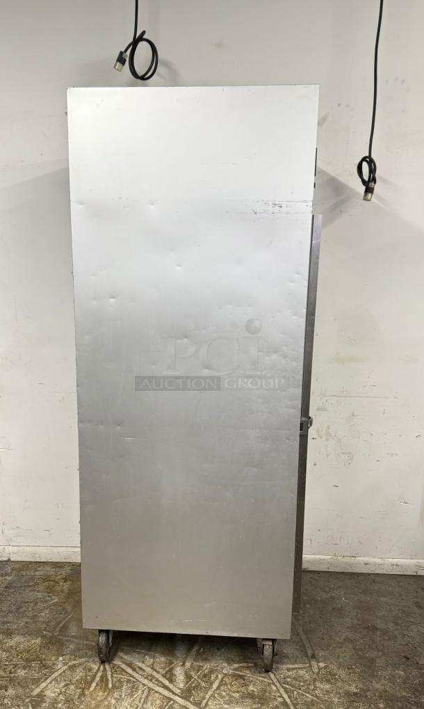 Metal industrial cabinet on wheels, scuffed surface, used condition. Cords visible, no labels or tags.