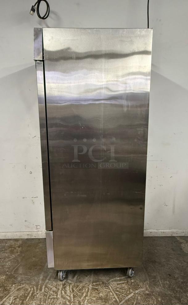 Stainless steel commercial refrigerator on casters, tall single-door, minor wear visible, cord attached.