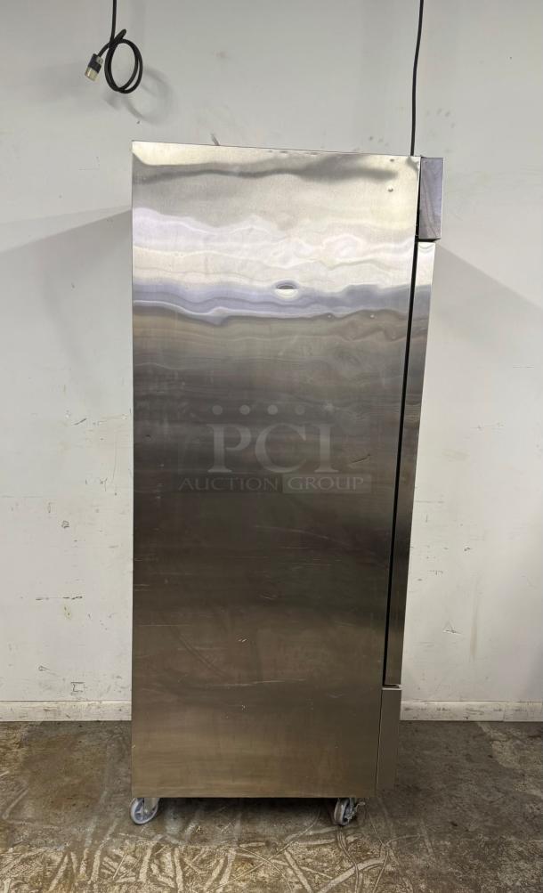 Stainless steel commercial refrigerator with casters, upright design, visible plug and cord, minor surface scratches.