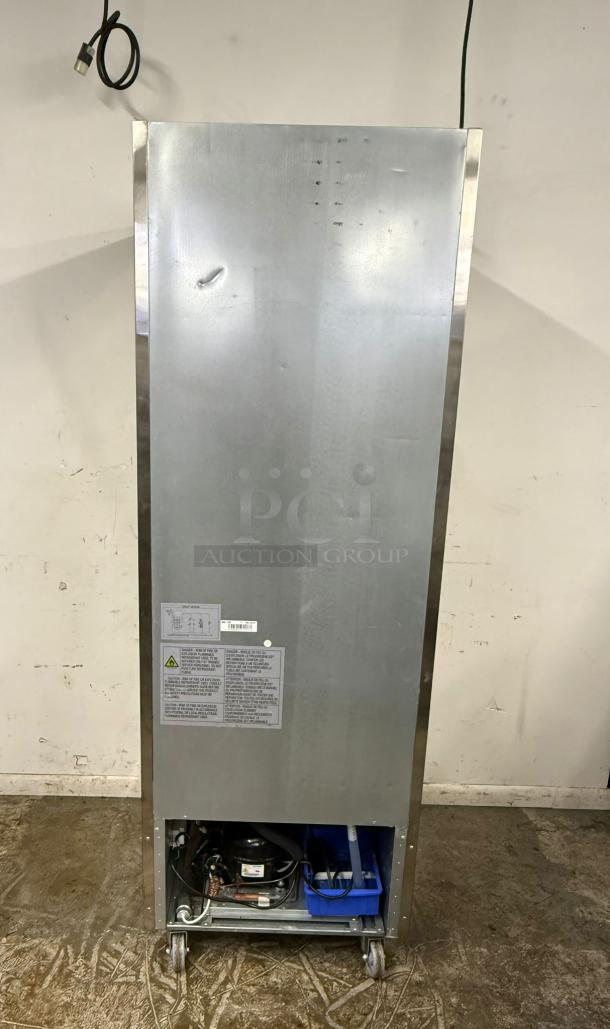 Commercial stainless steel refrigerator, floor model. Includes visible compressor unit and caution labels. Some exterior dents noted.