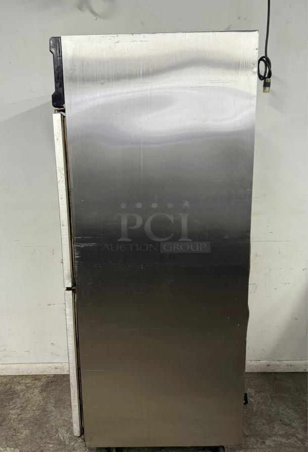Stainless steel commercial refrigerator, upright design, visible wear with scratches and dented panels, power cord attached.