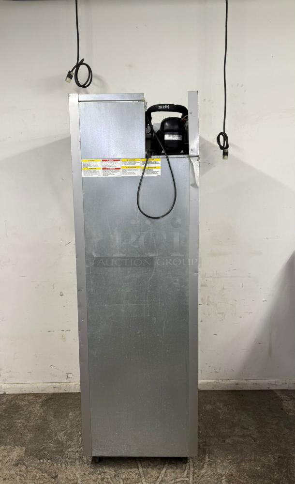 Tall metal commercial appliance with electrical plug, visible compressor, and safety warning labels. Good condition.