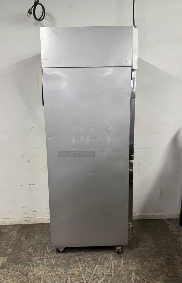 Commercial stainless steel refrigerator on wheels, showing moderate wear, with power cable attached.