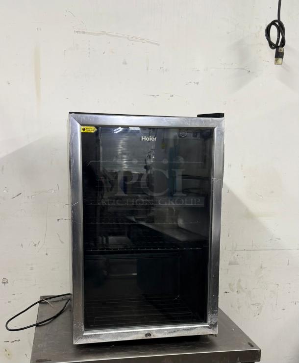 Haier mini fridge with glass door, black interior, shelving. Used condition, visible scratches. Energy efficiency label visible.