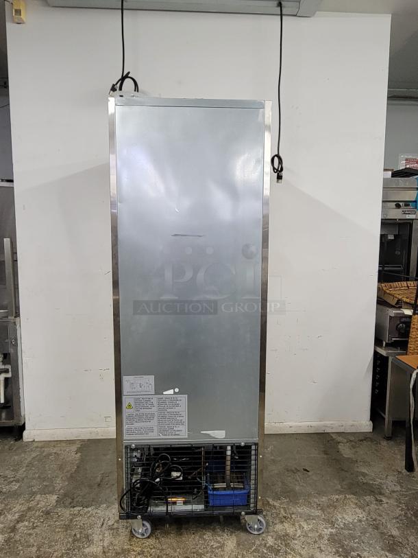 Commercial stainless steel refrigerator, rear view, with visible power cord and compressor. Label includes safety warnings.