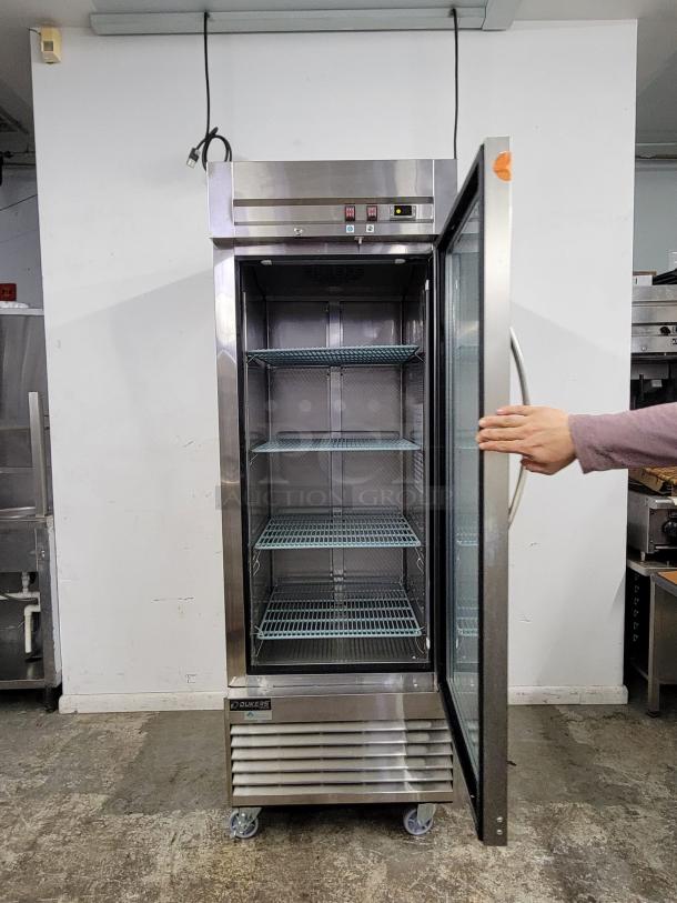 Commercial stainless steel freezer with three adjustable wire shelves, glass door, and digital temperature controls. Brand: Duke.