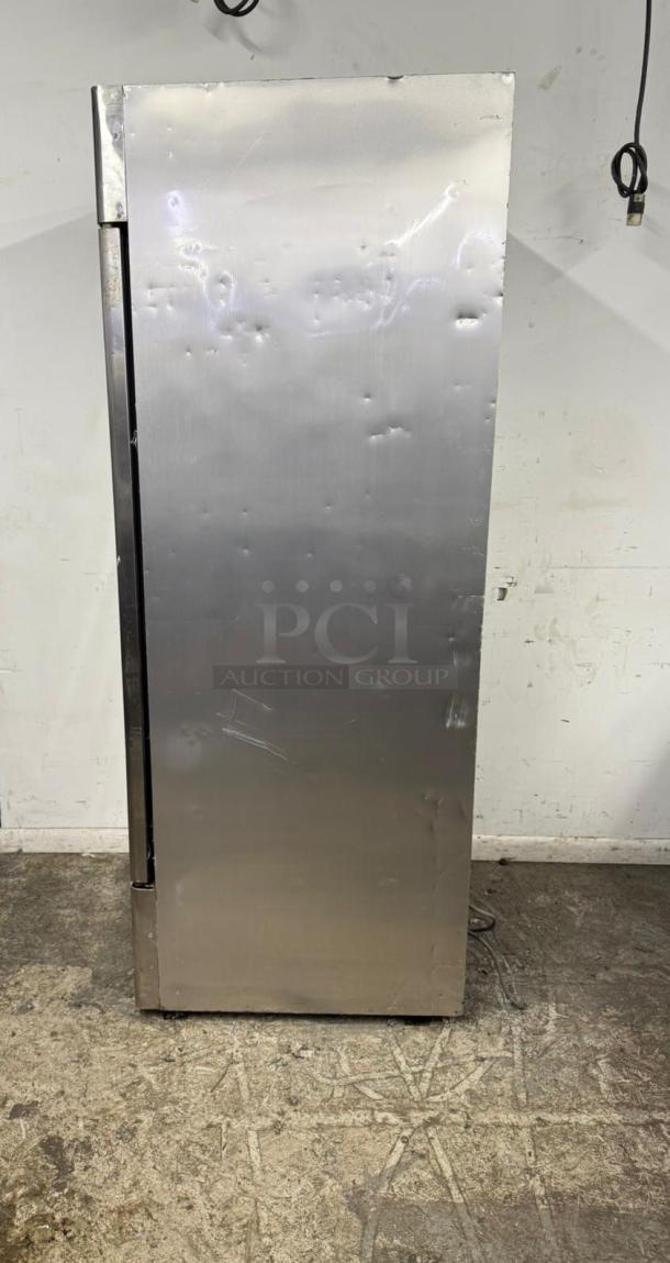 Commercial stainless steel refrigerator with visible dents and scratches, industrial setting. No visible labels or tags.
