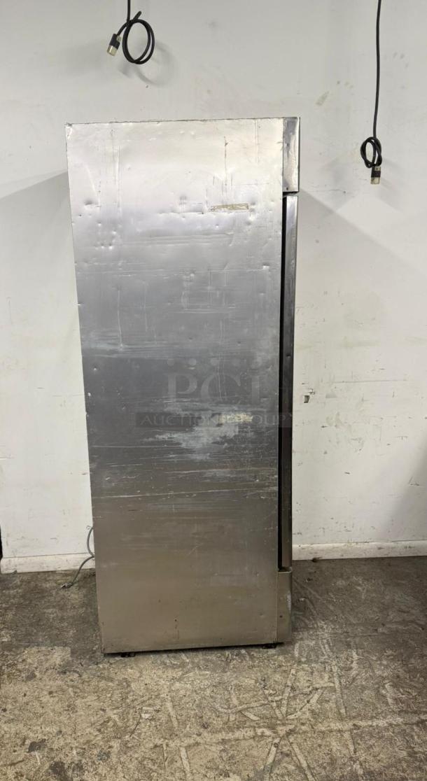 Stainless steel commercial refrigerator, showing signs of wear, with visible power cord and no identifiable branding or labels.