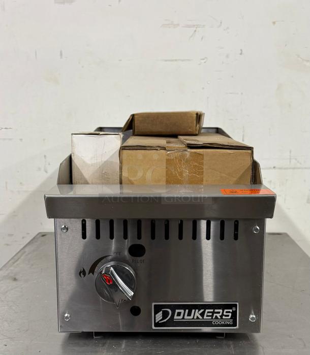 Dukers stainless steel cooking appliance with control knob, vent slits, and logo. Used condition with cardboard boxes on top.
