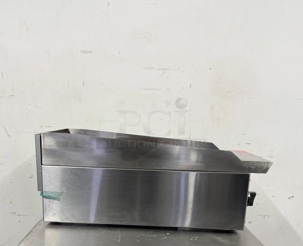Stainless steel griddle with slight wear, control knob on side, and a small piece of tape. Suitable for commercial use.