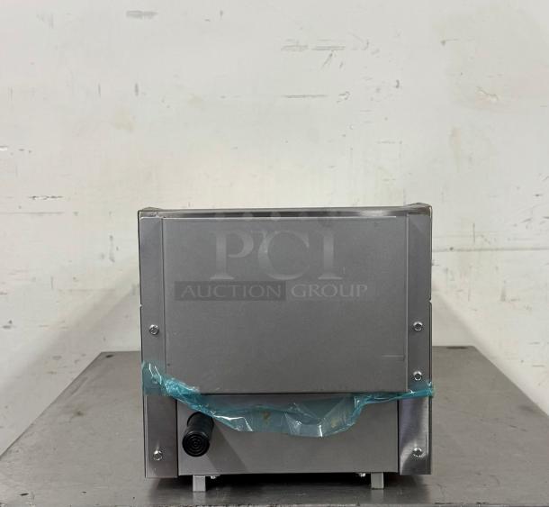 Stainless steel appliance, boxy shape, with a black power input. Wrapped in protective blue plastic. Clean, good condition.