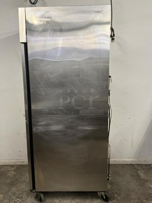 Stainless steel commercial refrigerator on wheels, used condition. Power cord visible, no visible branding or labels.