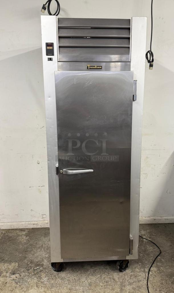 Traulsen commercial stainless steel refrigerator, single door, with top ventilation, wheels, and power cord, showing slight wear.
