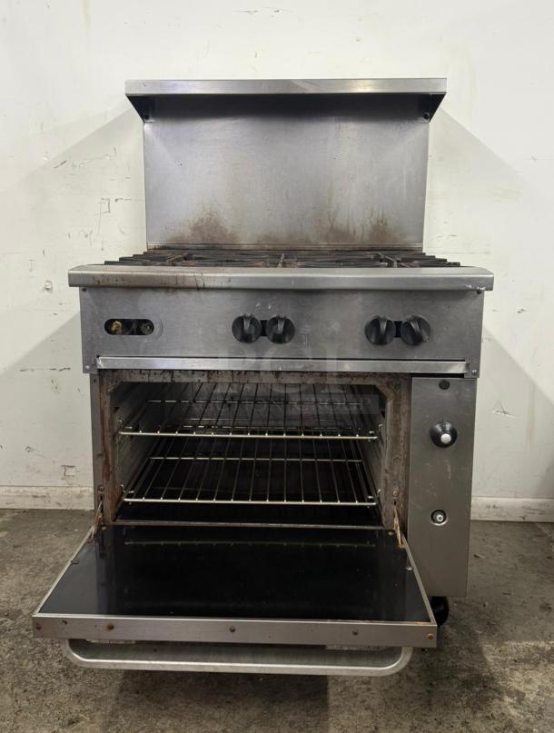 Commercial stainless steel gas range with four burners and an oven, showing signs of use, with two oven racks.