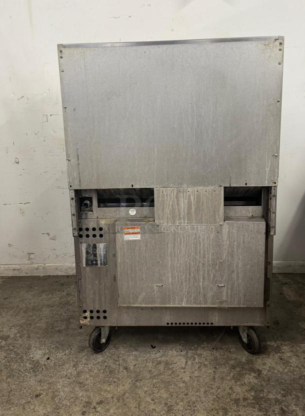 Industrial ice machine on casters, showing moderate wear. Visible caution label and manufacturer’s tag on lower panel.