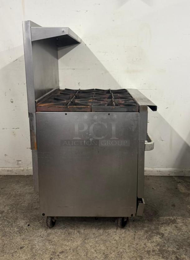 Industrial stainless steel gas stove with six burners, used condition, visible wear and rust, mobile with wheels.