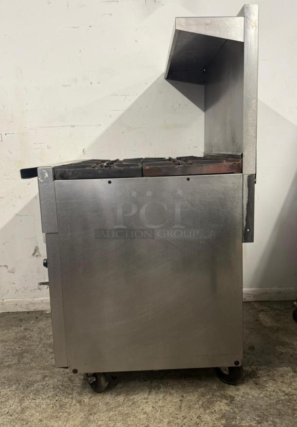 Commercial stainless steel stove with overhead shelf, dual burners, used condition, on wheels for mobility.
