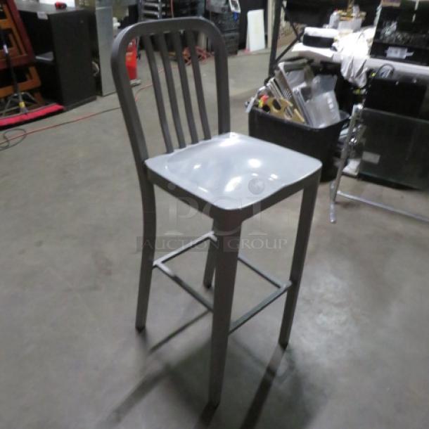 Aluminum bar height patio chair with slatted back and curved seat, in used condition. Ideal for outdoor seating areas.
