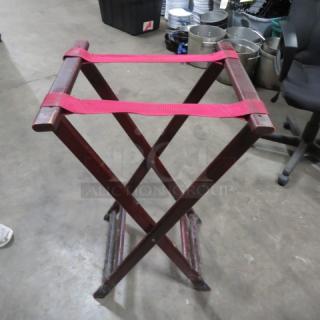Wooden tray stand with red straps, foldable design, sturdy condition, suitable for holding trays or luggage.