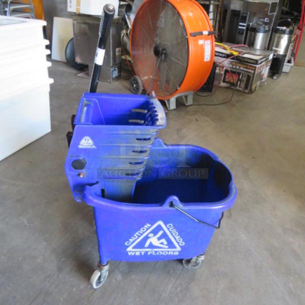 Blue mop bucket with wringer, "Caution Wet Floors" label, on wheels, good condition, ideal for cleaning tasks.