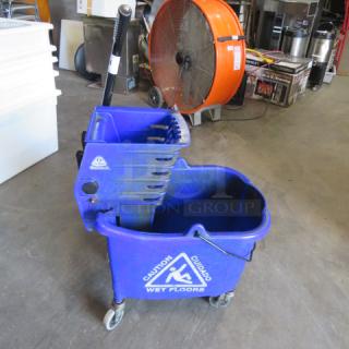 Blue mop bucket with wringer, "Caution Wet Floors" label, on wheels, good condition, ideal for cleaning tasks.