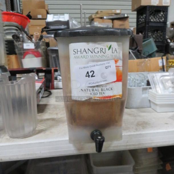 Beverage dispenser with tap, labeled "Shangrila Award Winning Tea, Natural Black Iced Tea," on a cluttered warehouse shelf.