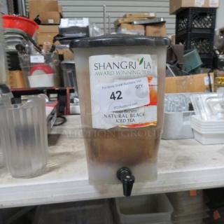 Beverage dispenser with tap, labeled "Shangrila Award Winning Tea, Natural Black Iced Tea," on a cluttered warehouse shelf.