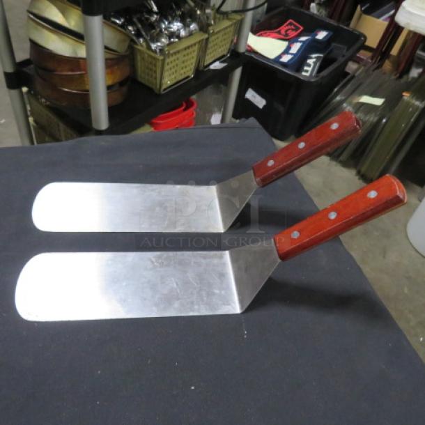 Set of two commercial hamburger turners with stainless steel blades and wooden handles. Appears in good condition.