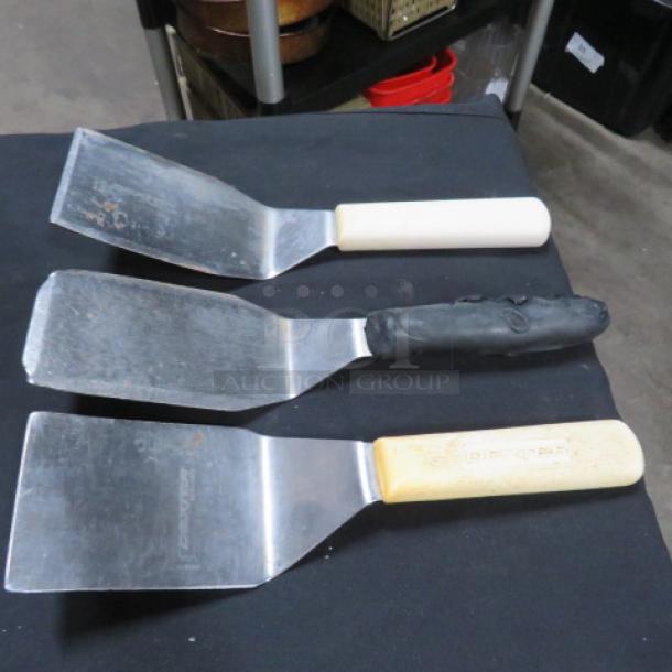 Three assorted commercial hamburger turners with stainless steel blades and varied handles; used condition.