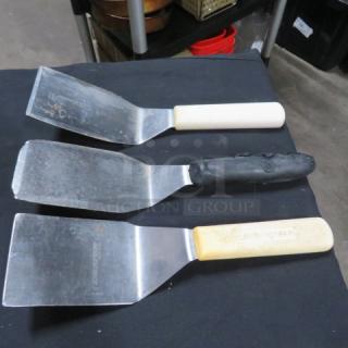 Three assorted commercial hamburger turners with stainless steel blades and varied handles; used condition.