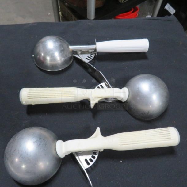 Three white handle dishers on black surface, with stainless steel scoops. Good condition, suitable for portioning tasks.