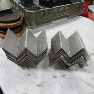 A large set of stainless steel taco holders, stacked on a table, in good condition.