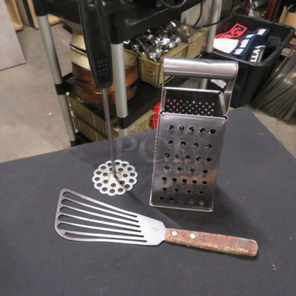 Assorted cooking utensils: metal slotted spatula, potato masher, and box grater. Used condition with visible wear.