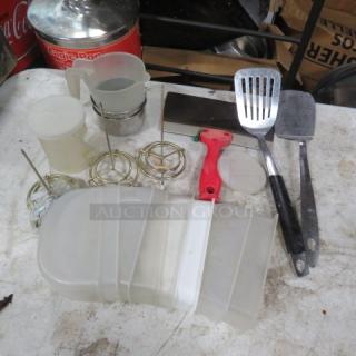 A collection of miscellaneous kitchen utensils and containers, including spatulas, plastic storage, and metal strainers, in used condition.
