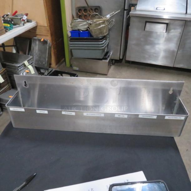 Stainless steel bottle rail, 24x4x6, in good condition, features labeled sections for organizing spirits or condiments.