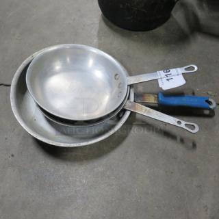 Three stacked sauté pans, assorted sizes, with visible wear. Blue handle on one and paper tag labeled "716."