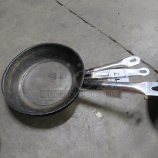 Assorted sauté pan set, showing signs of use, metal handles, tagged "3XBID", suitable for various cooking needs.