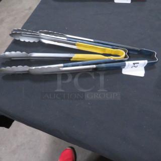 Set of assorted tongs on a black surface. Includes stainless steel and silicone grips. Auction tag marked "27".