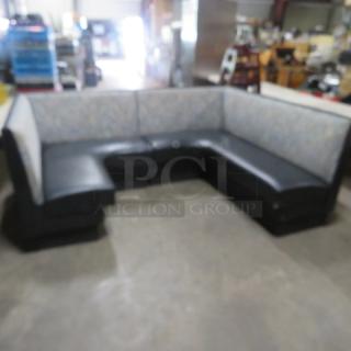 C-shaped booth with black cushioned seat and patterned cushioned back, in good condition, ideal for dining or lounge areas.