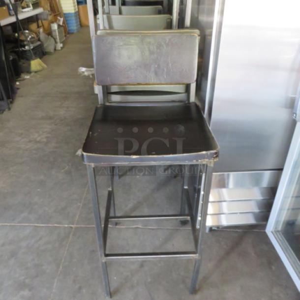 Metal bar height chair with wooden seat and back, footrest, visible wear, suitable for indoor bars or kitchens.