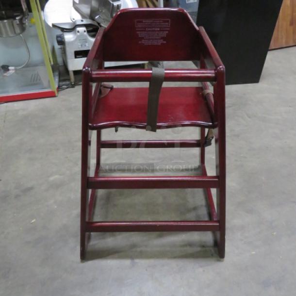 Wooden high chair with safety straps, red finish, sturdy construction. Features safety warnings on backrest. Excellent condition.