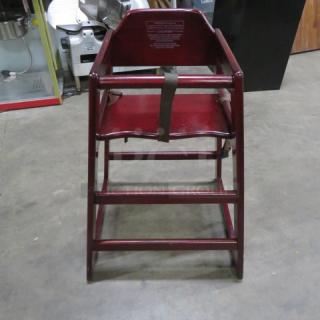 Wooden high chair with safety straps, red finish, sturdy construction. Features safety warnings on backrest. Excellent condition.