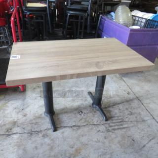 Brown tabletop with dual black pedestal bases, measuring 48x30x30 inches. Used condition with a visible label.