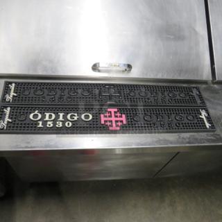 Black Codigo 1530 bar mat with raised lettering and pink logo, in good condition. Ideal for bartops.