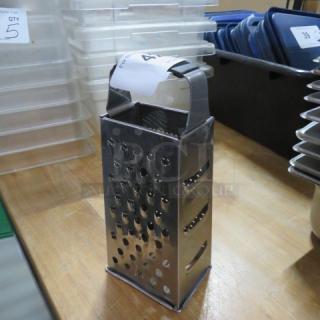 Metal box grater with four sides on a wooden surface, features various grating options; small label on handle.