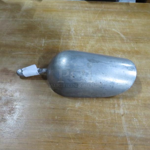85oz aluminum scoop on wooden surface, showing wear consistent with use. Small white tag attached to handle.